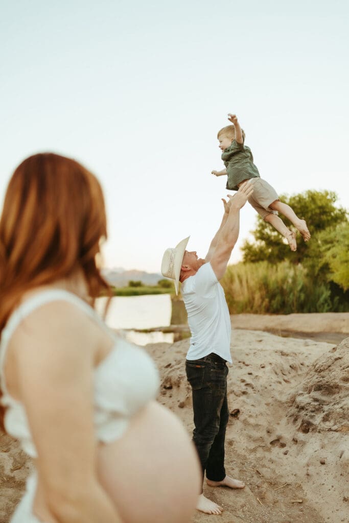Dad lifting his toddler into the air during a sunset maternity photography session at Phon D Sutton Recreation Area.