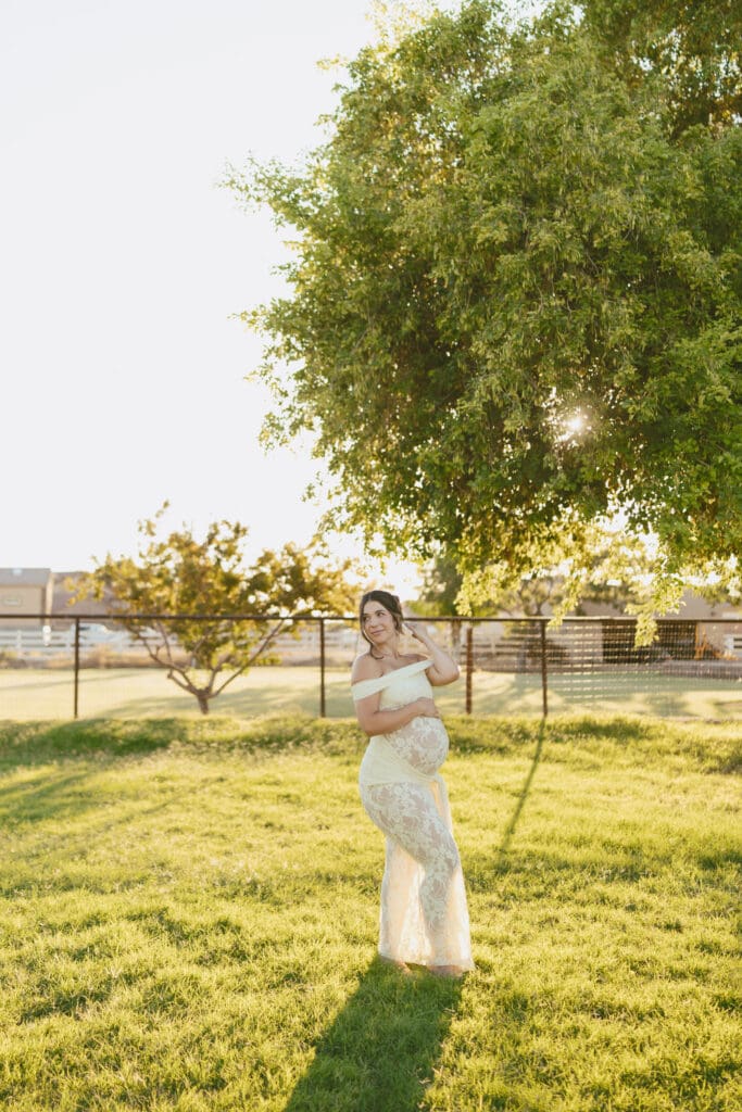 Expecting mother in a cream lace maternity gown standing beneath a large tree at Patch of Paradise AZ.