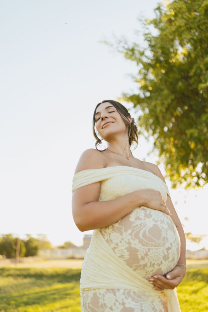 Outdoor maternity portrait of an expecting mother in a cream lace dress at a Gilbert farm location.