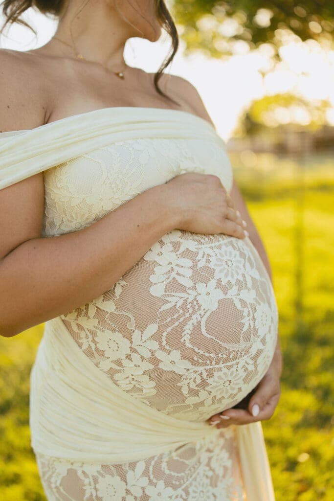 Close-up of a pregnant belly in a lace maternity gown during a golden hour maternity session.