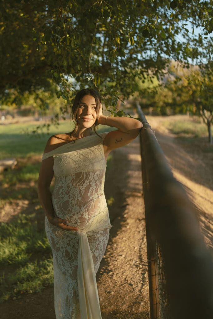 Expecting mother leaning against a fence during a peaceful maternity photography session in Queen Creek.