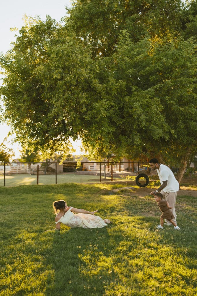Father playing with his toddler while expecting mother smiles during an outdoor family maternity session near Queen Creek.