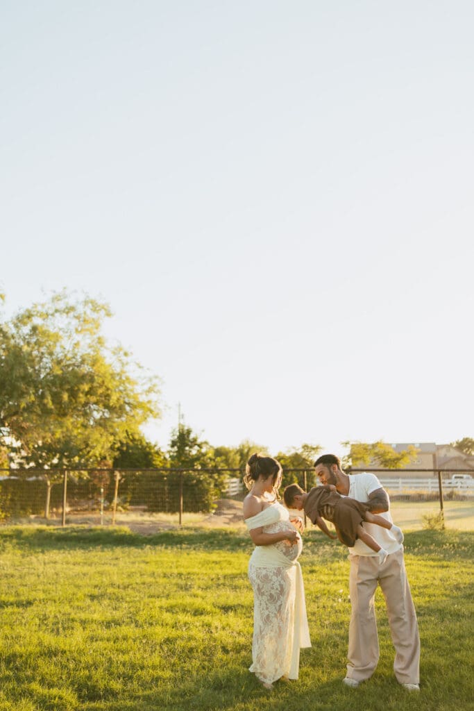 Expecting parents sharing a candid moment beneath leafy trees during a maternity session near Queen Creek.