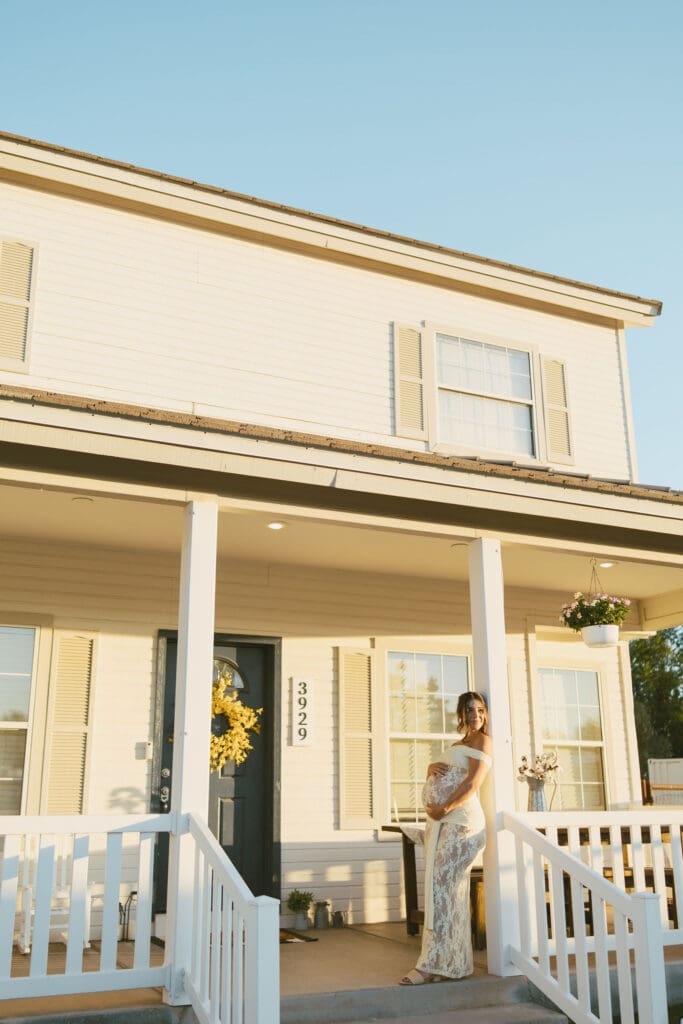 Expecting mother smiling on the front porch of Patch of Paradise AZ during a maternity photography session.