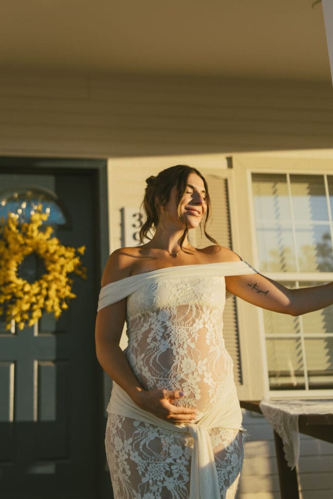 Expecting mother smiling on the front porch of Patch of Paradise AZ during a maternity photography session.