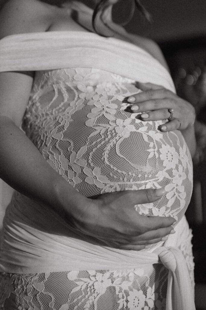 Close-up black and white maternity photo of an expecting mother's baby bump in a lace maternity gown.