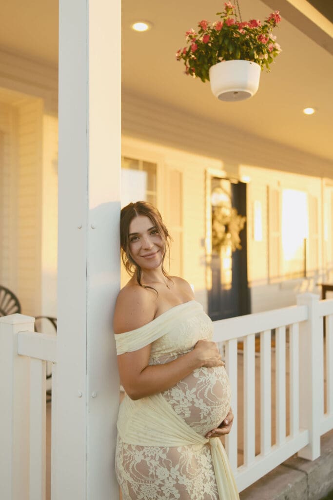 Pregnant mother smiling while leaning against a white porch railing during a golden hour maternity session in Gilbert, Arizona.