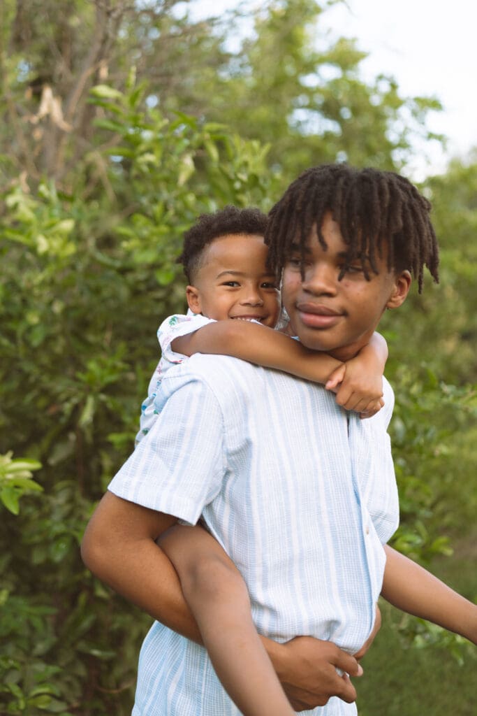 Older brother giving his little brother a piggyback ride during a family photo session at Hagen Farms in Queen Creek.