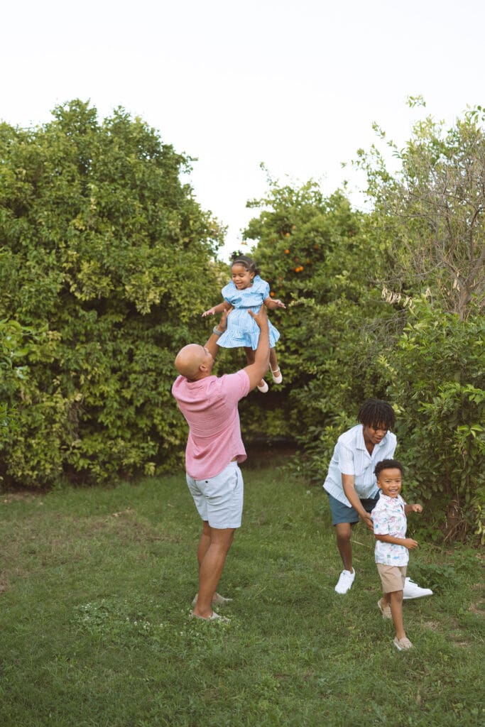 Dad lifting his daughter into the air during a fun family photo session in a Queen Creek citrus orchard.