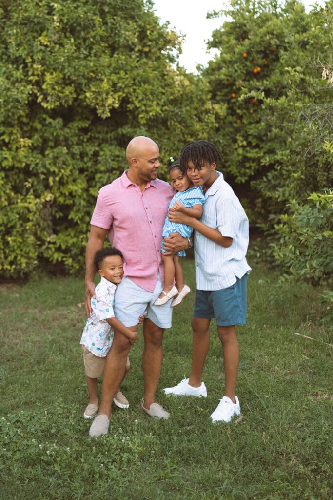 Family of four posing together in a lush orchard during a Queen Creek family photography session.