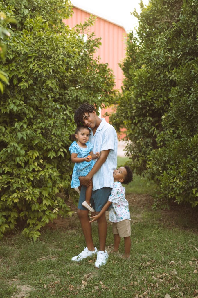 Teenage brother holding his little sister while standing in a citrus orchard at Hagen Farms.