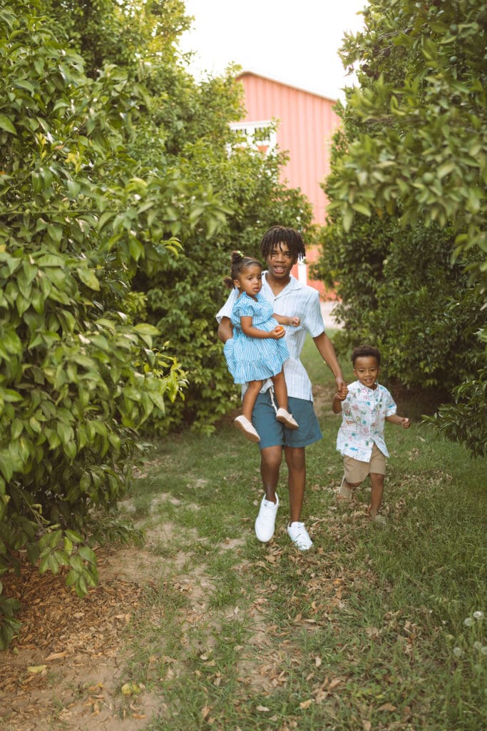 Older brother carrying his little sister while walking through a Queen Creek citrus orchard during family photos.