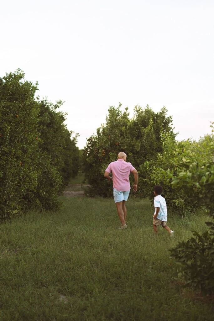 Father and son walking through a lush citrus orchard during a Queen Creek family photo session.