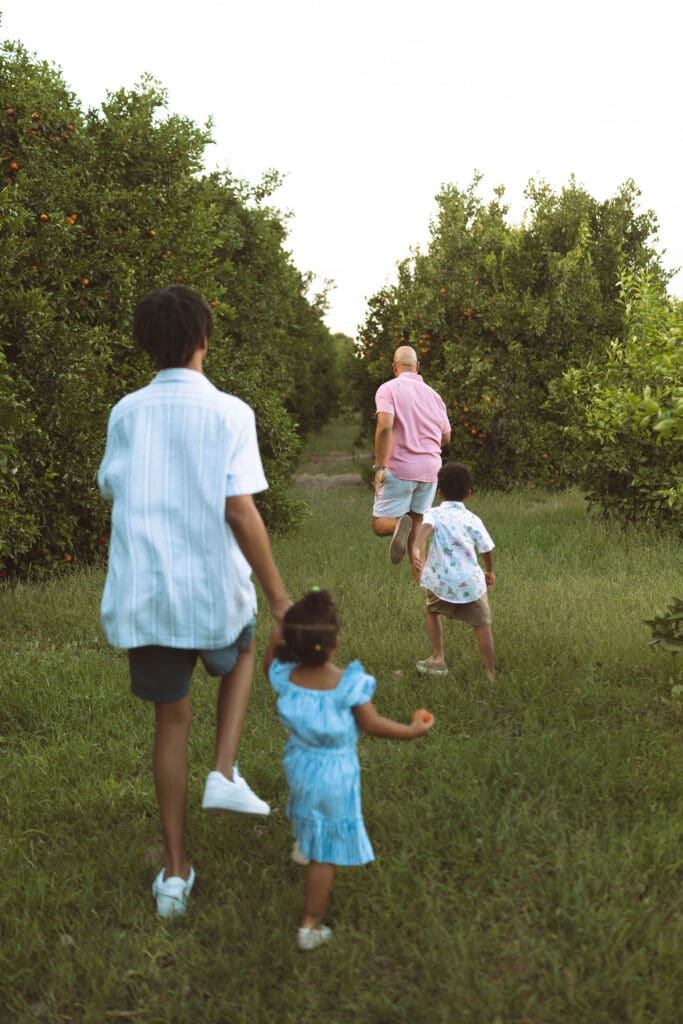 Siblings walking through the citrus orchard with their father during a family photography session near Gilbert and Queen Creek.