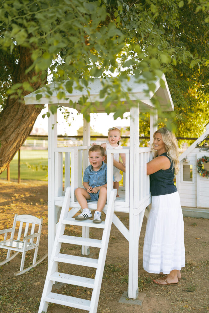 Little boy climbing into a white treehouse during a relaxed Gilbert family photography session at a beautiful green outdoor location.