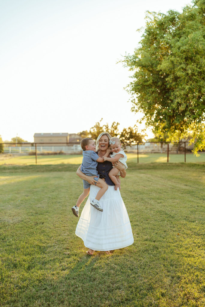 Mother carrying her two young children during a candid outdoor family photography session in Gilbert.