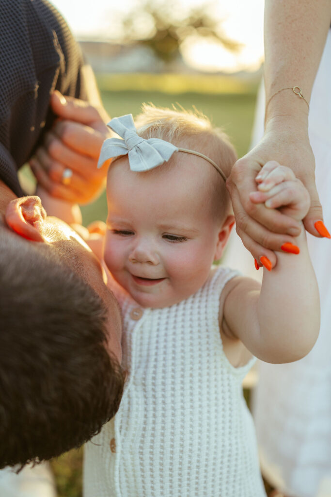 Close-up of a smiling baby holding her parents' hands during a natural family photography session in Gilbert.