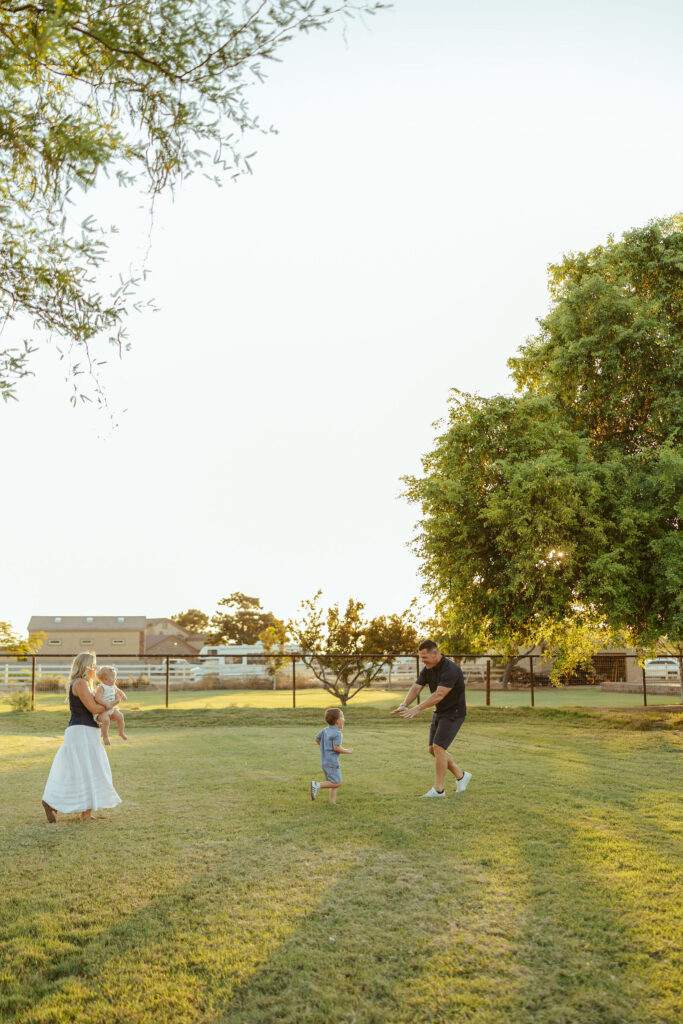 Father playing chase with his son while mom holds their daughter during an outdoor family session in Gilbert.