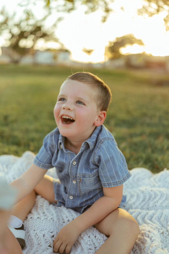 Smiling little boy sitting on a blanket during a relaxed outdoor family photo session in Gilbert.