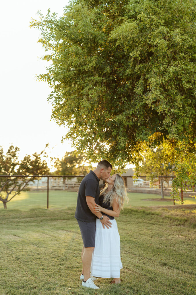 Couple sharing a quiet embrace beneath a large tree during a natural outdoor family session in Gilbert, Arizona.