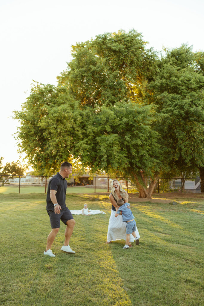Parents playing with their young children on a green lawn during a candid Gilbert family photography session.