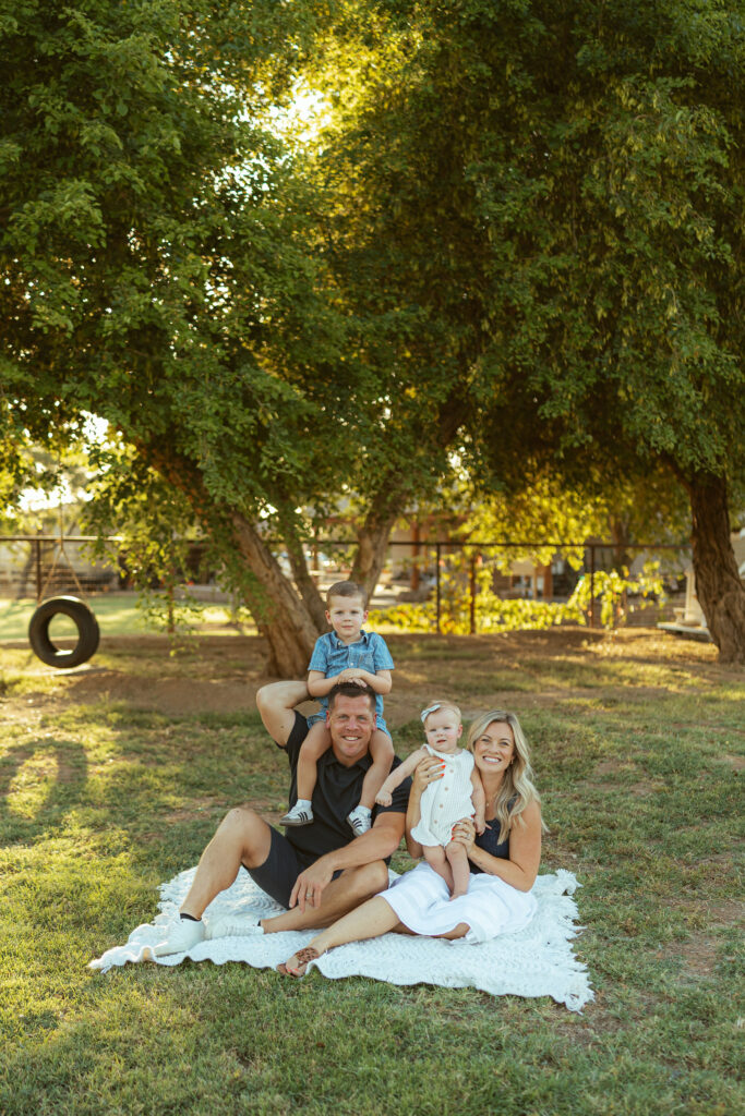 Family sitting together on a blanket beneath a large shade tree during a golden hour family photography session in Gilbert, Arizona.