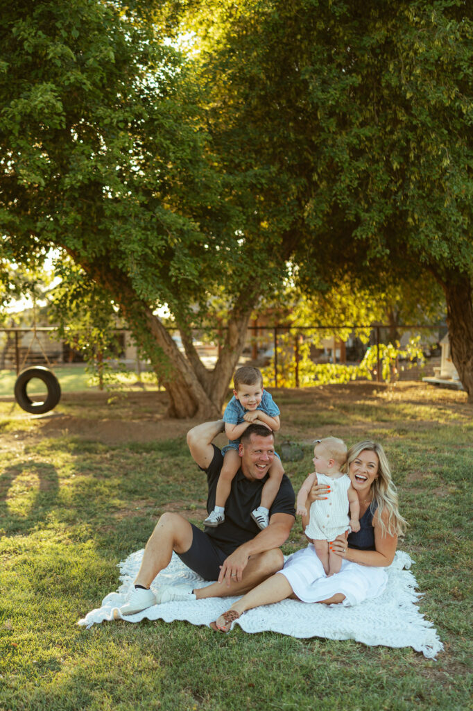Family laughing together beneath a large shade tree during a golden hour Gilbert family photography session.