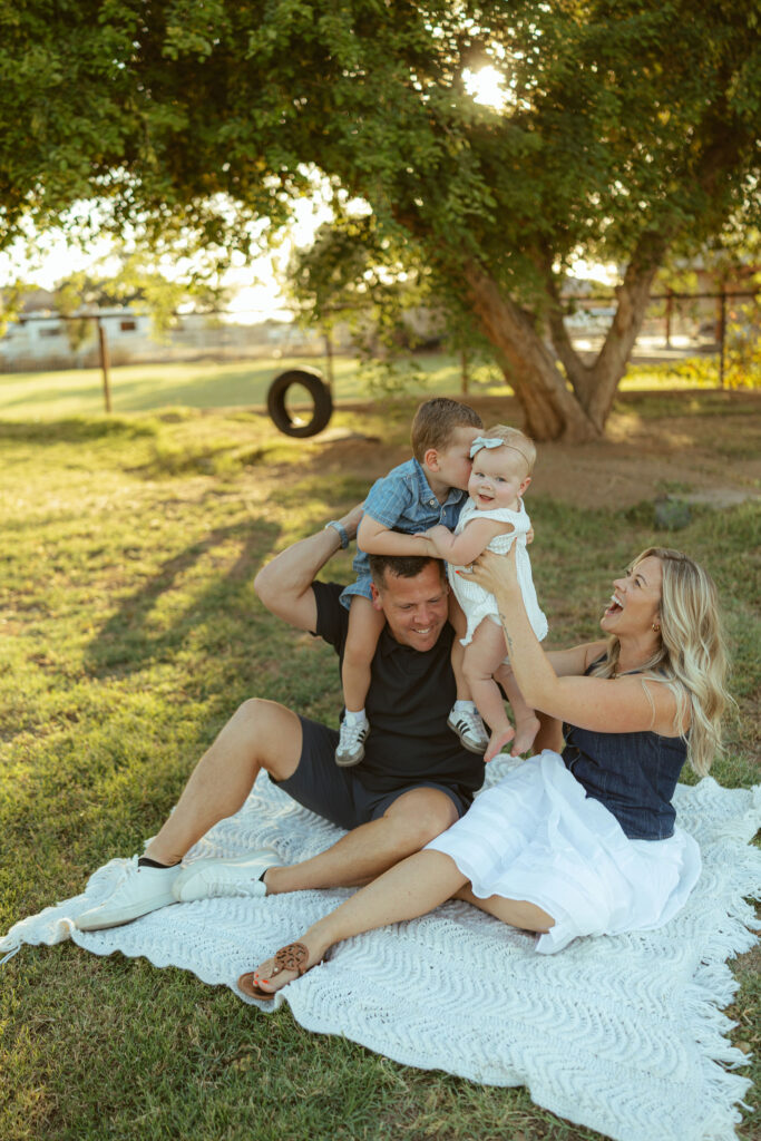 Family laughing together on a picnic blanket beneath a large shade tree during a Gilbert family photography session.