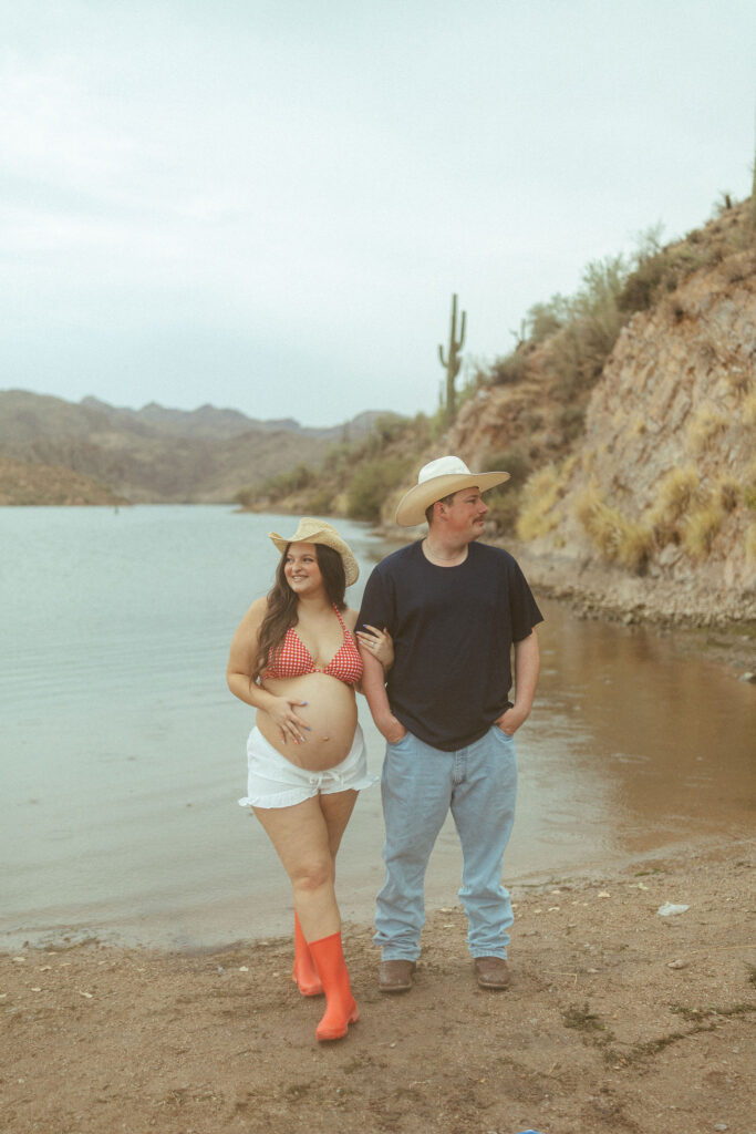 Couple walking hand in hand along the shoreline at Butcher Jones Beach during a relaxed maternity photography session near Saguaro Lake.