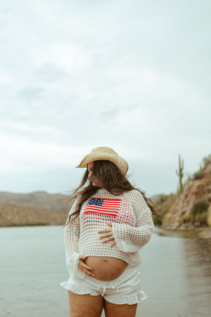 Expecting mother wearing a patriotic crochet sweater over her baby bump during a summer maternity session at Butcher Jones Beach in Mesa.