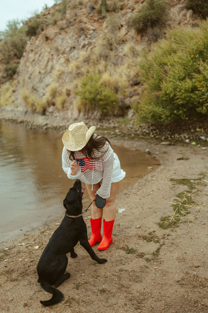 Pregnant mother bending down to pet her black Labrador during a lakeside maternity session in Mesa, Arizona.