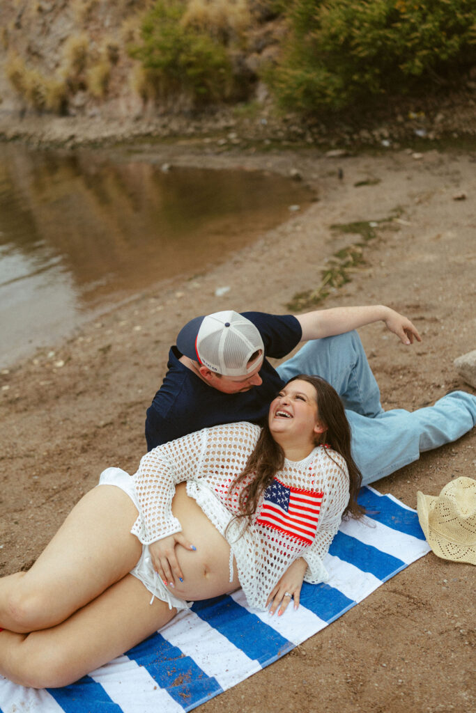 Couple relaxing on a picnic blanket along the shoreline during a romantic maternity session at Saguaro Lake.