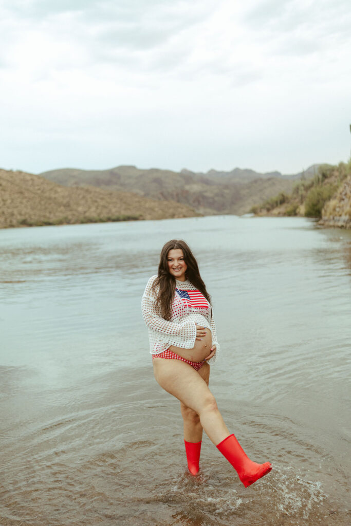 Pregnant mother standing barefoot in the water at Butcher Jones Beach during a summer maternity photography session near Saguaro Lake.