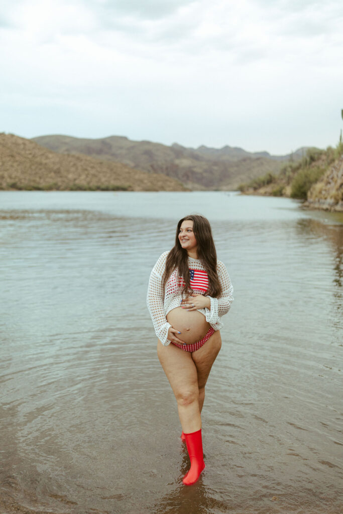 Pregnant mother wearing a patriotic crochet sweater while standing in the shallow water at Saguaro Lake during a summer maternity session.