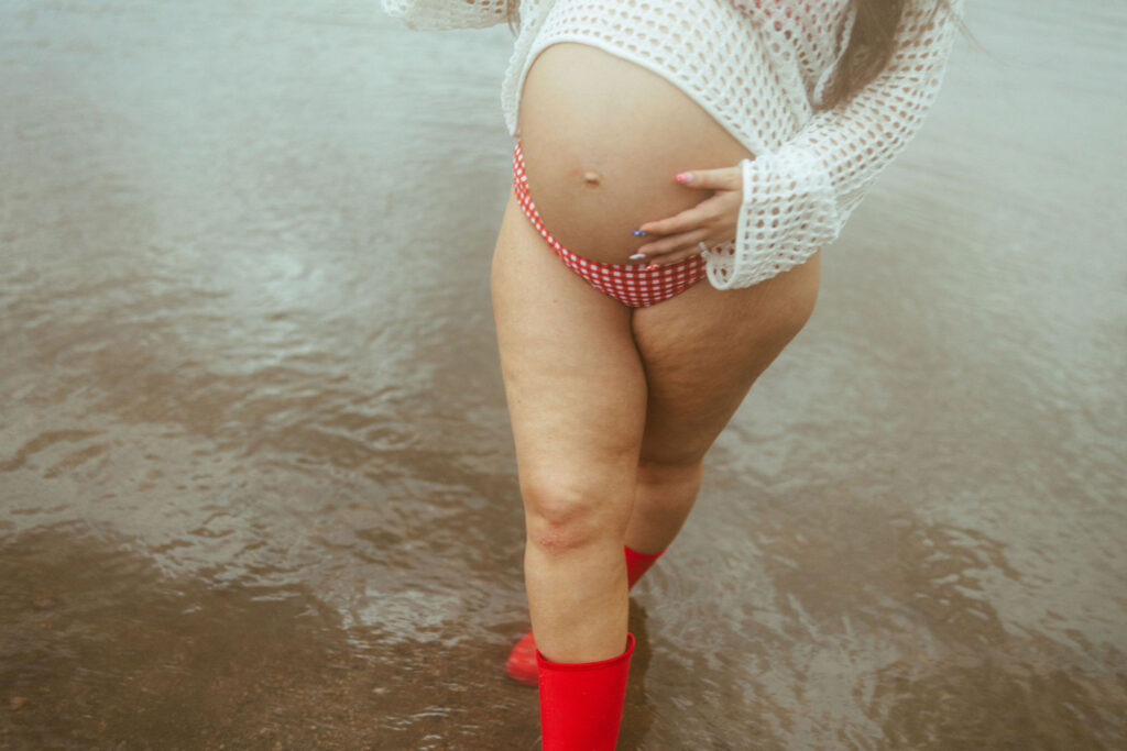 Close-up of an expecting mother's baby bump while walking through the water during a lakeside maternity session at Butcher Jones Beach.