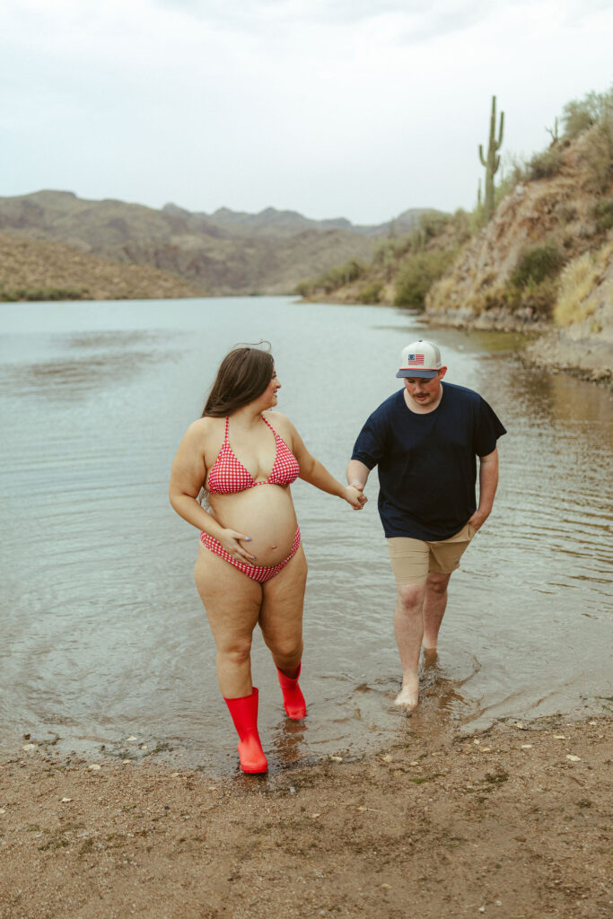 Couple holding hands while walking through the water during a relaxed maternity session at Saguaro Lake near Mesa, Arizona.