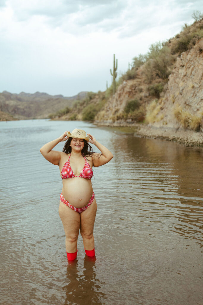 Pregnant mother adjusting her cowboy hat while standing in the water during a Butcher Jones Beach maternity session.