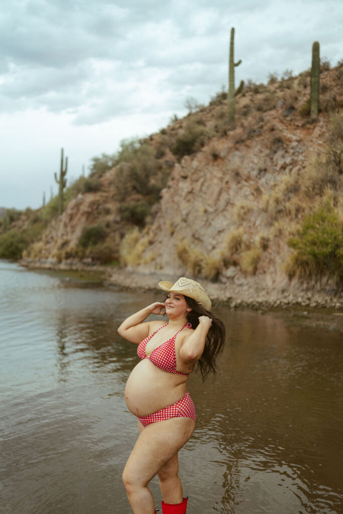 Pregnant mother posing in the water beneath dramatic desert skies during a maternity session at Butcher Jones Beach.