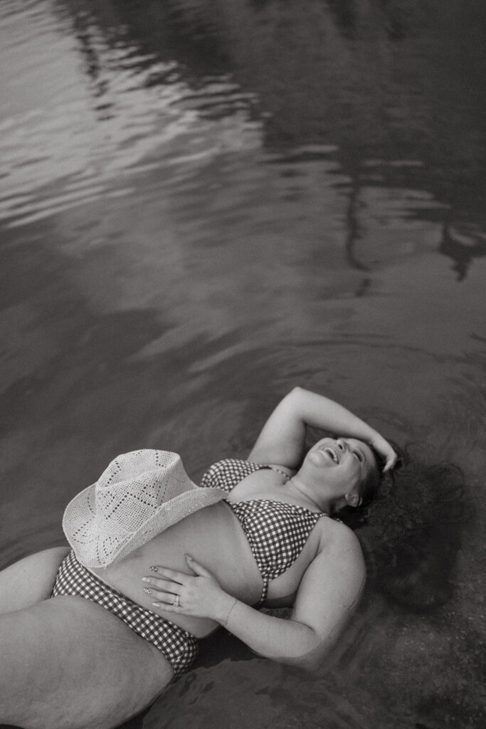 Artistic black and white portrait of an expecting mother resting in the water during a lakeside maternity session at Butcher Jones Beach.
