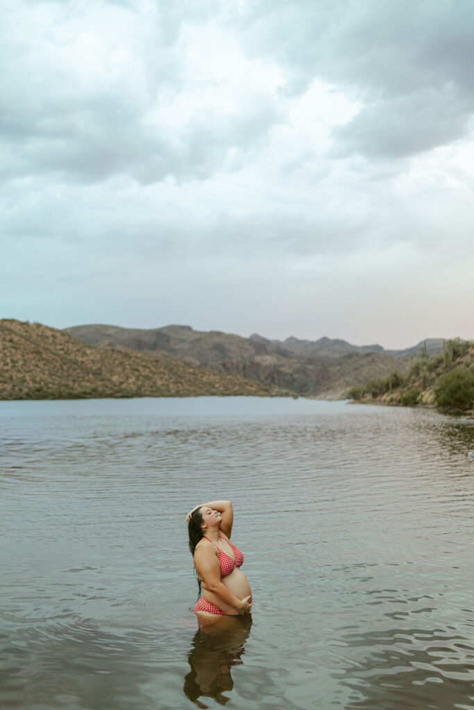 Pregnant mother standing in the water beneath dramatic desert skies during a maternity photography session at Butcher Jones Beach.