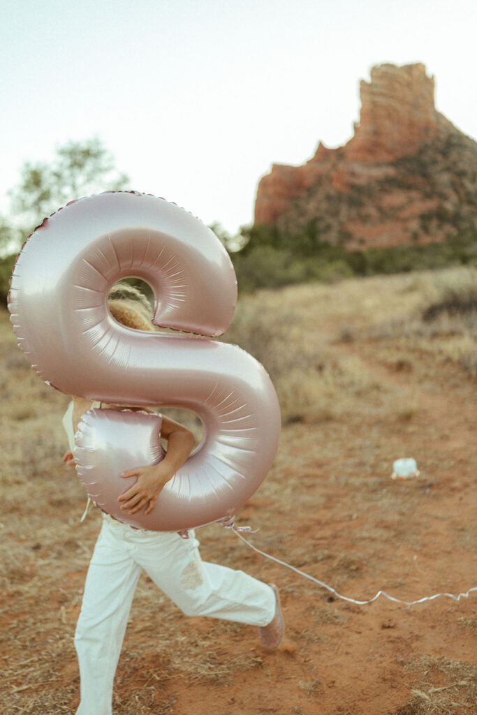 Child holding a large silver birthday balloon during a family photo session in Sedona, Arizona with red rock scenery behind them.