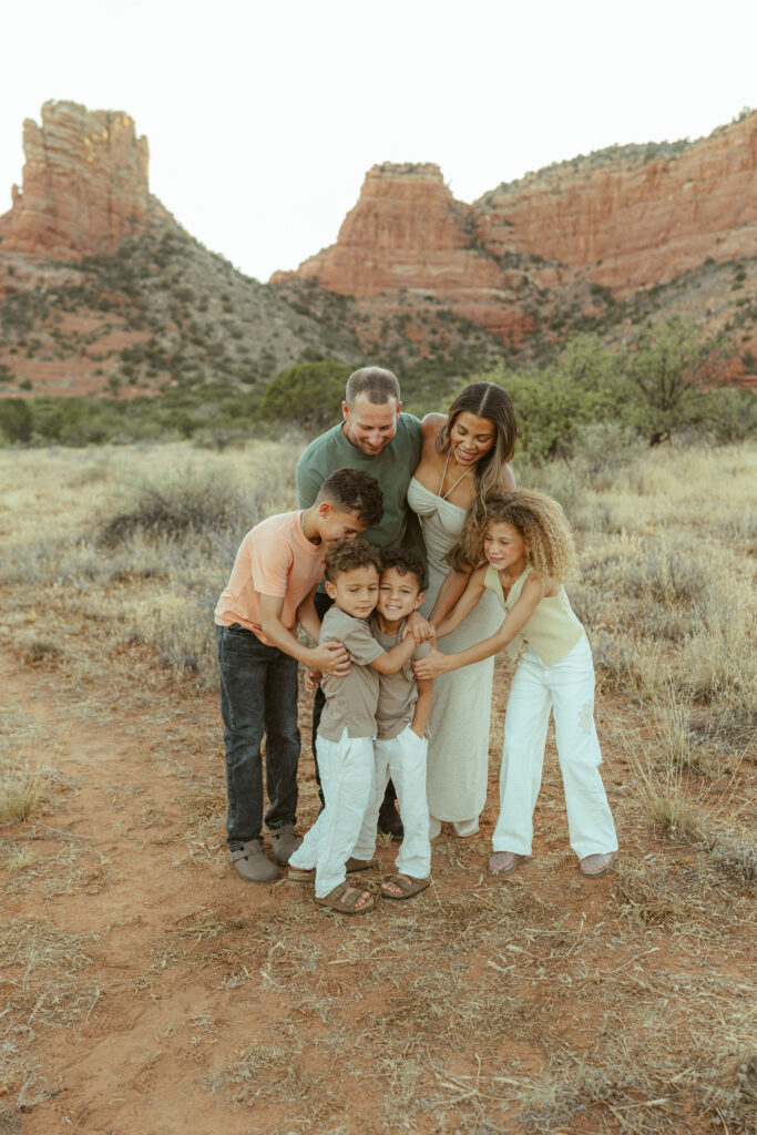 Family of six laughing together during a playful outdoor family photography session in Sedona with iconic red rock views in the background.