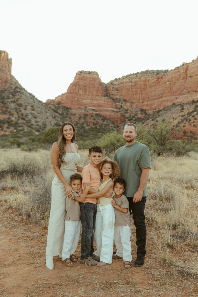 Family portrait in Sedona featuring parents and four children standing together in front of Cathedral Rock at golden hour.
