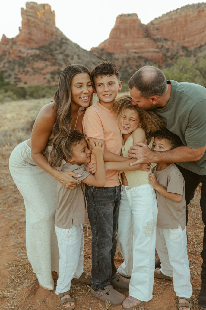 Close-up family hug during a Sedona family photography session capturing genuine smiles and connection with red rocks softly blurred in the background.