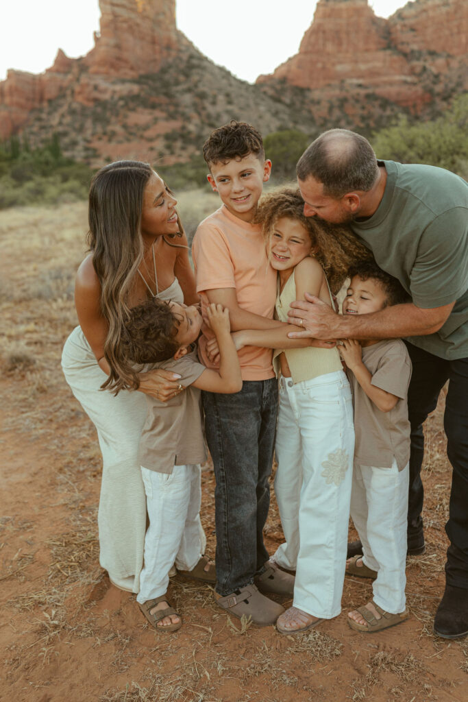 Family group hug during a Sedona family photography session with genuine smiles and Cathedral Rock softly visible in the background.