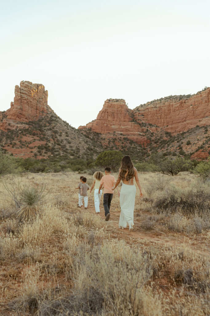 Sedona family vacation photos capturing a family walking together through the desert with Cathedral Rock in the background during golden hour.
