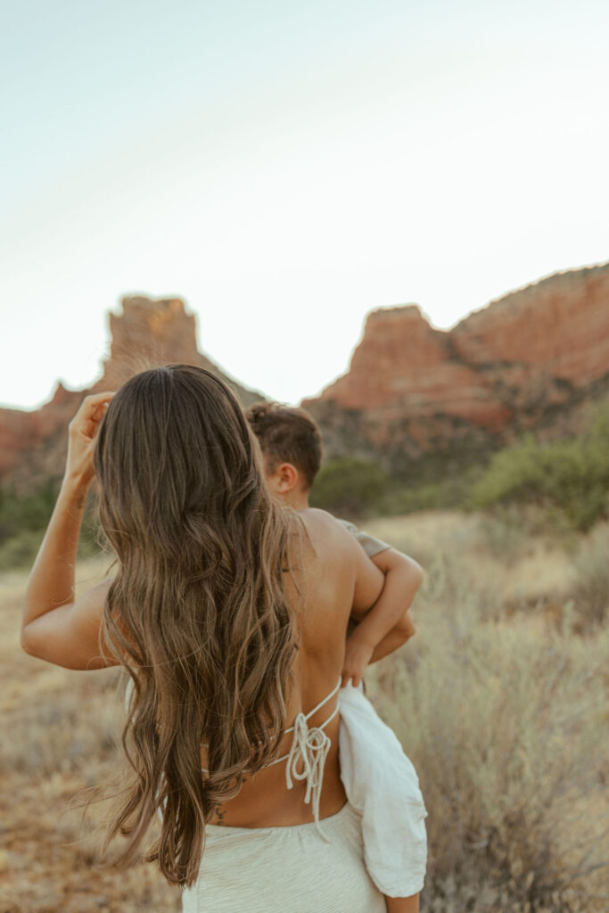 Mother carrying her son during a sunset family photo session in Sedona with dramatic red rock views behind them.