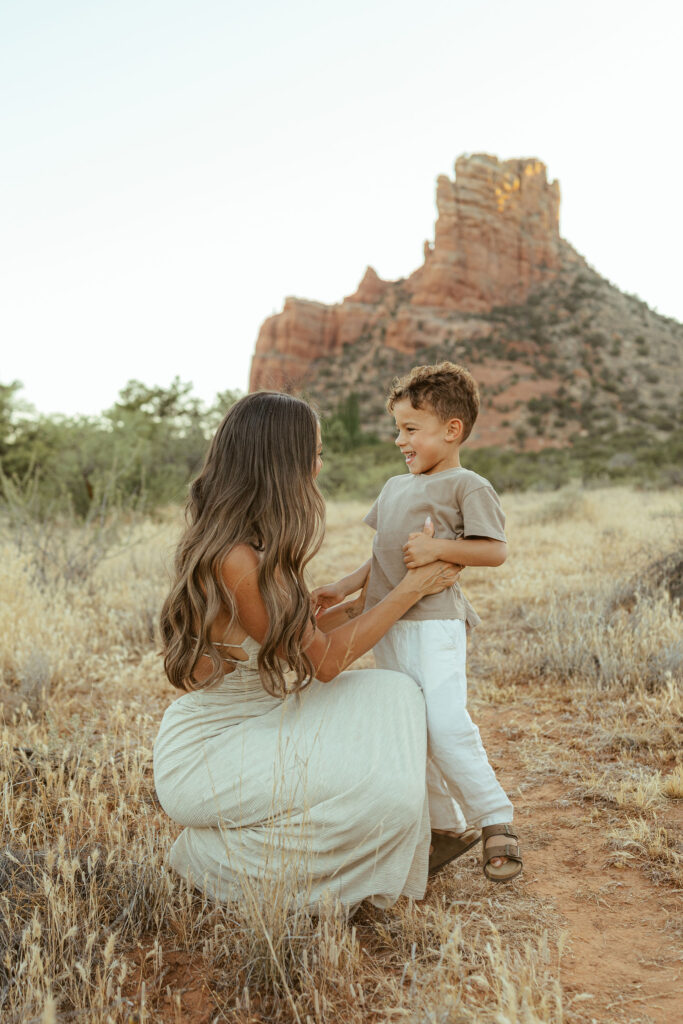 Mother smiling at her young son during a natural family photography session in Sedona surrounded by Arizona's iconic red rocks.