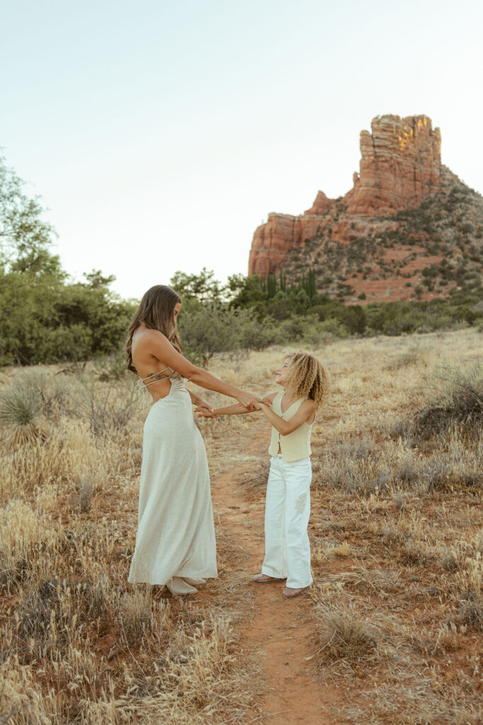 Mother and daughter holding hands during a candid family photography session in Sedona featuring Arizona's iconic red rock scenery.