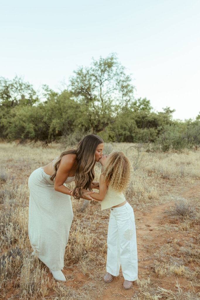 Mother kissing her daughter during a heartfelt outdoor family photo session in Sedona surrounded by the natural Arizona desert.